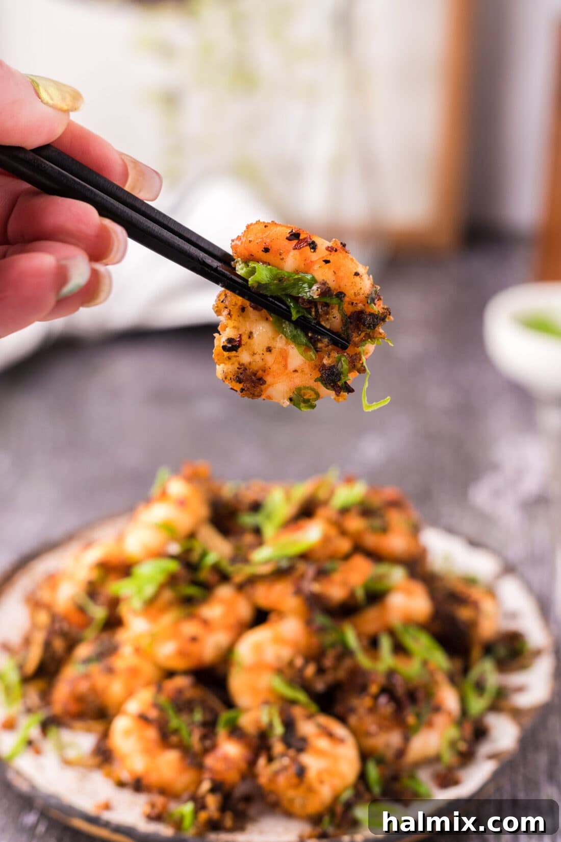 Chopsticks gracefully holding a perfectly golden and crispy salt and pepper shrimp, ready to be enjoyed.