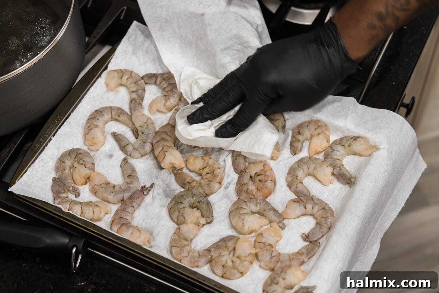 Patting raw shrimp dry with a paper towel on a cutting board, preparing them for seasoning.