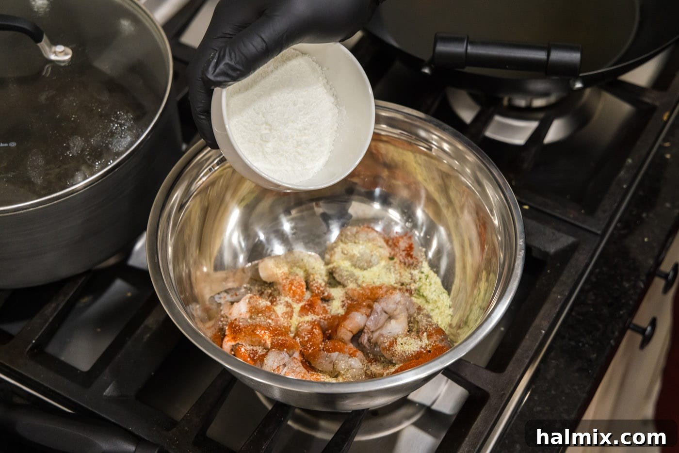 Adding a scoop of cornstarch to a bowl of seasoned raw shrimp.
