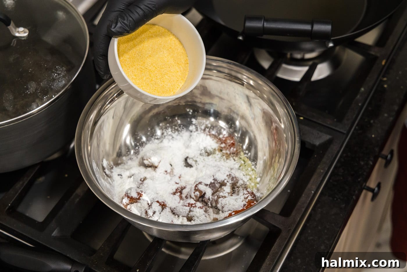 Adding a scoop of yellow cornmeal to a bowl of shrimp already coated with cornstarch.