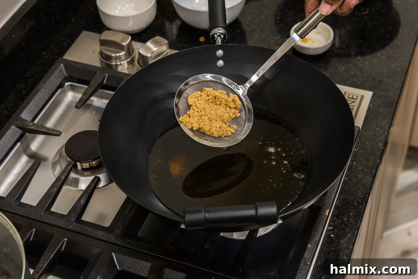 Adding minced garlic to shimmering hot oil in a wok.