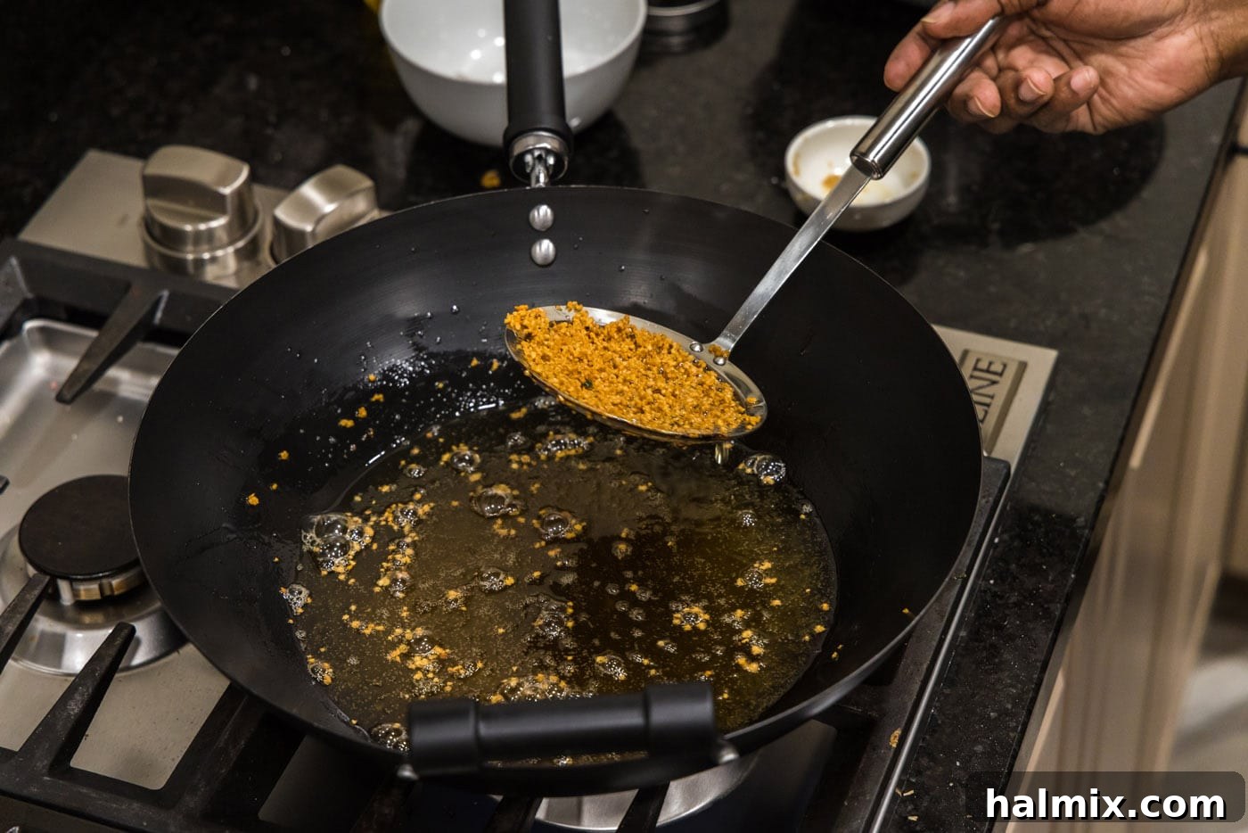 Removing crispy fried garlic from the hot oil in a wok using a fine mesh strainer.