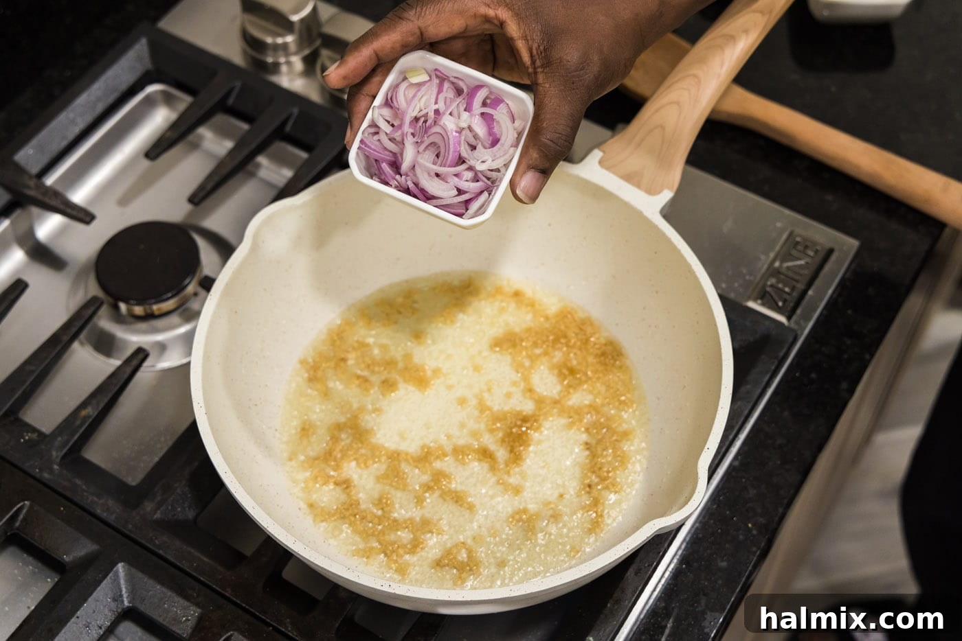 Adding chopped shallots to a skillet with sizzling garlic and olive oil.