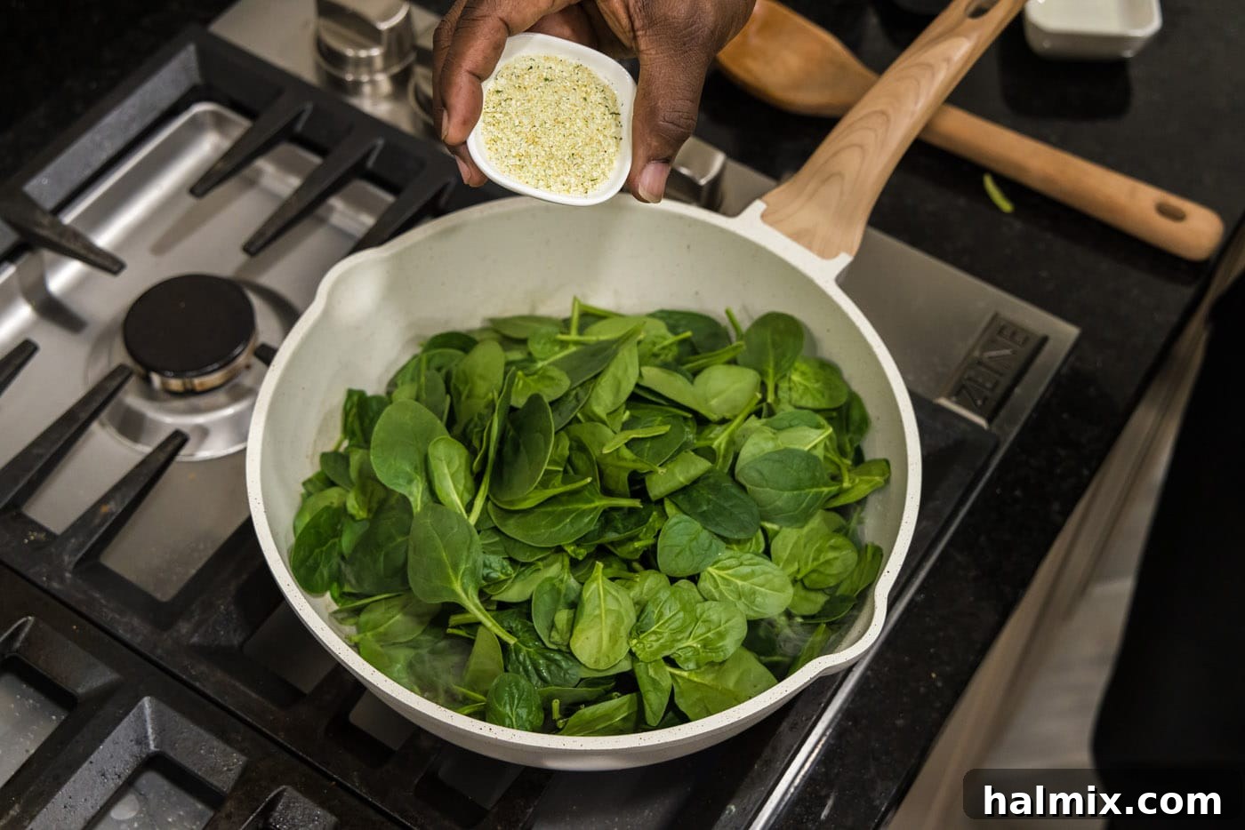 Seasoning a mound of fresh spinach leaves with garlic salt in a skillet.