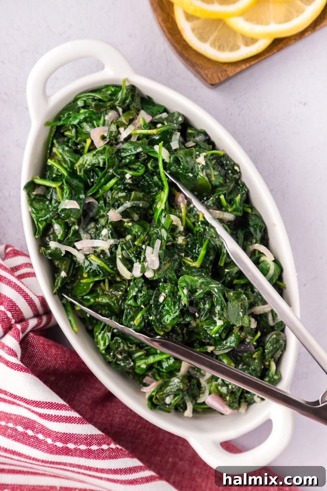 A vibrant serving of Sautéed Spinach arranged on a platter with serving tongs.