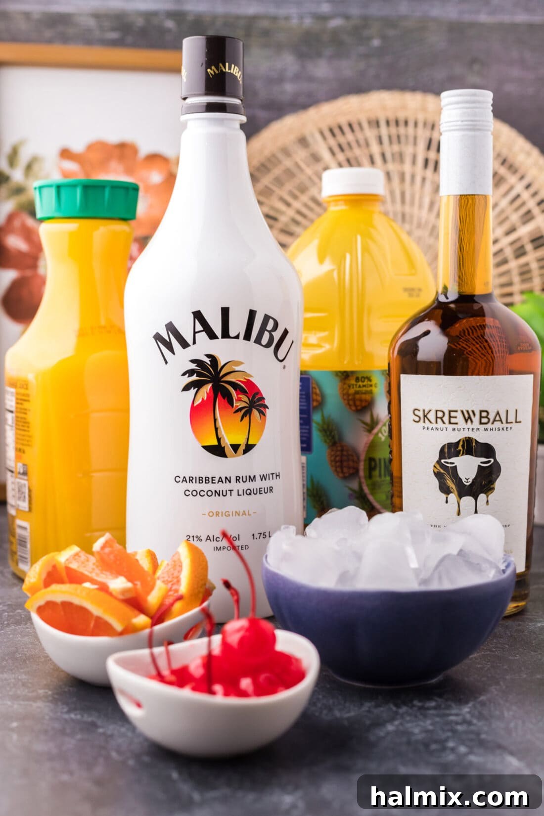 A collection of ingredients for the Skrew Loose Cocktail, including Skrewball whiskey, coconut rum, orange juice, and pineapple juice.