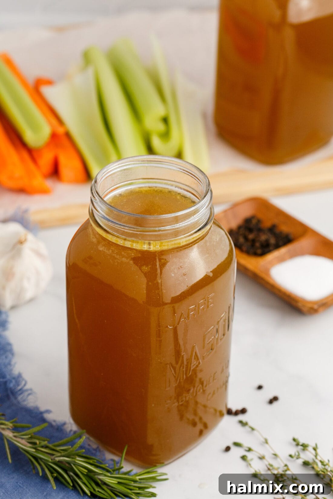 A jar of rich homemade chicken stock with fresh carrots and celery in the background, highlighting the fresh ingredients.