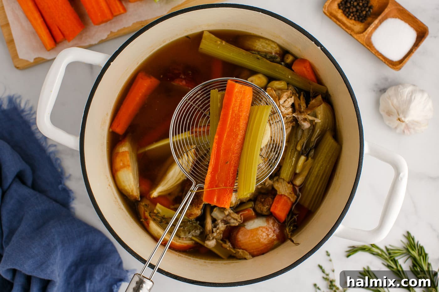 Straining cooked vegetables from the chicken stock using a fine-mesh strainer.
