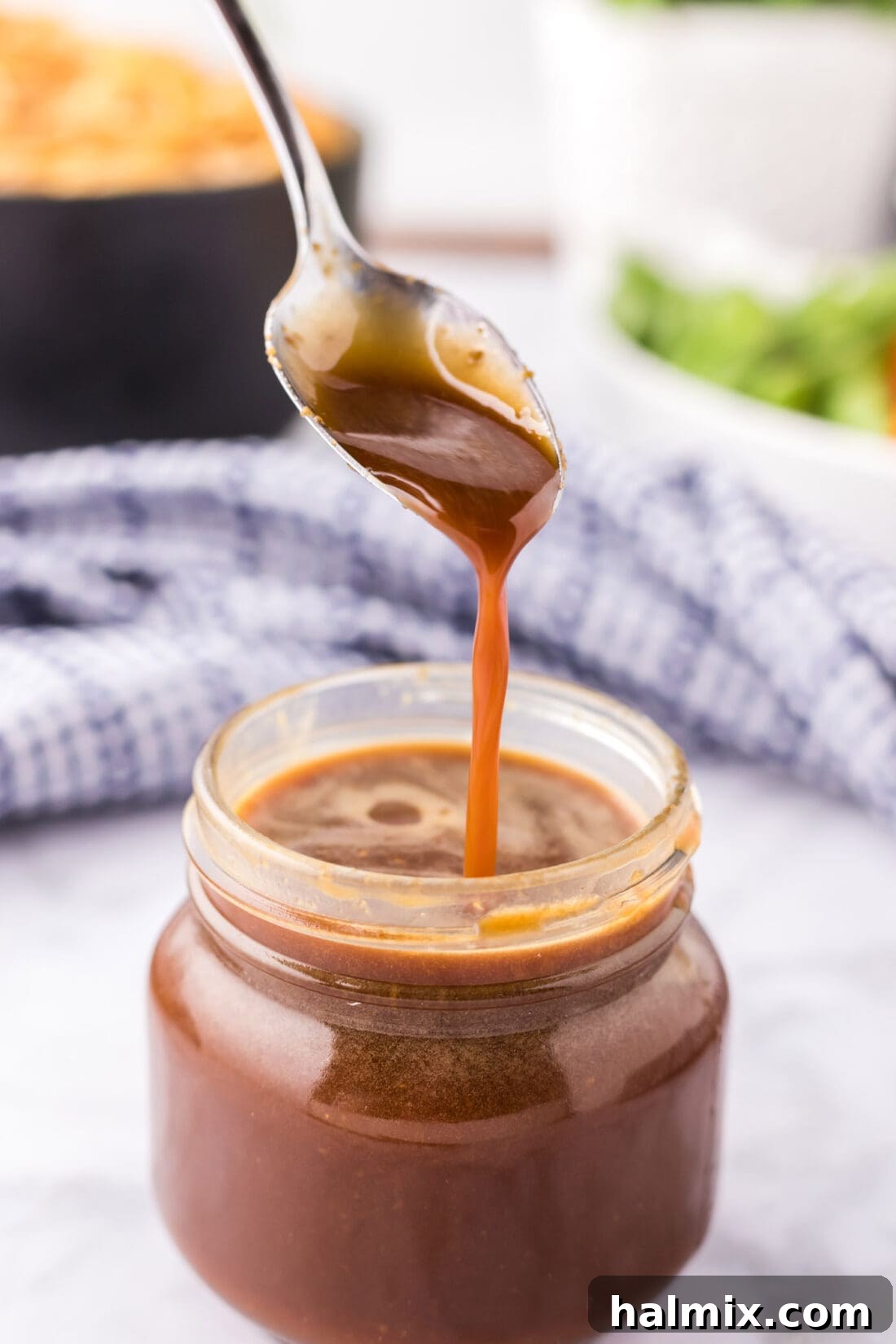 A stream of rich, homemade teriyaki sauce pouring from a spoon into a glass jar, showcasing its beautiful sticky glaze texture.
