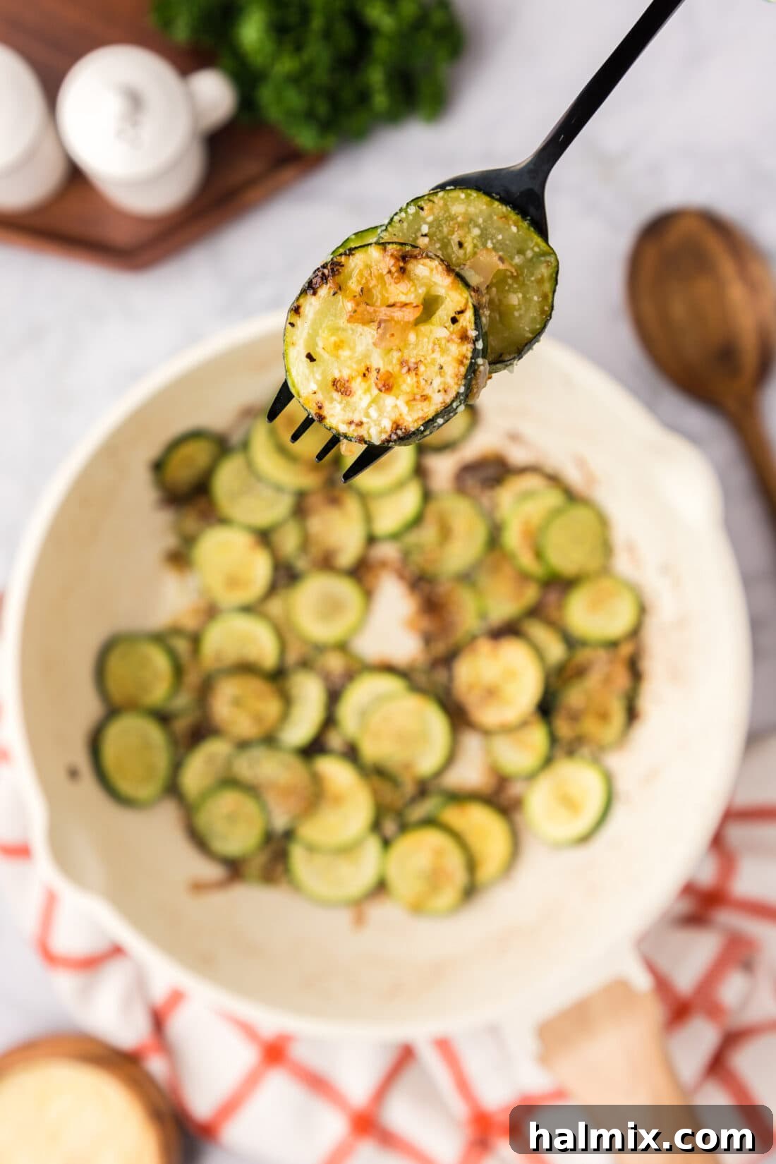 Sautéed Zucchini on a fork held above a skillet of Sautéed Zucchini
