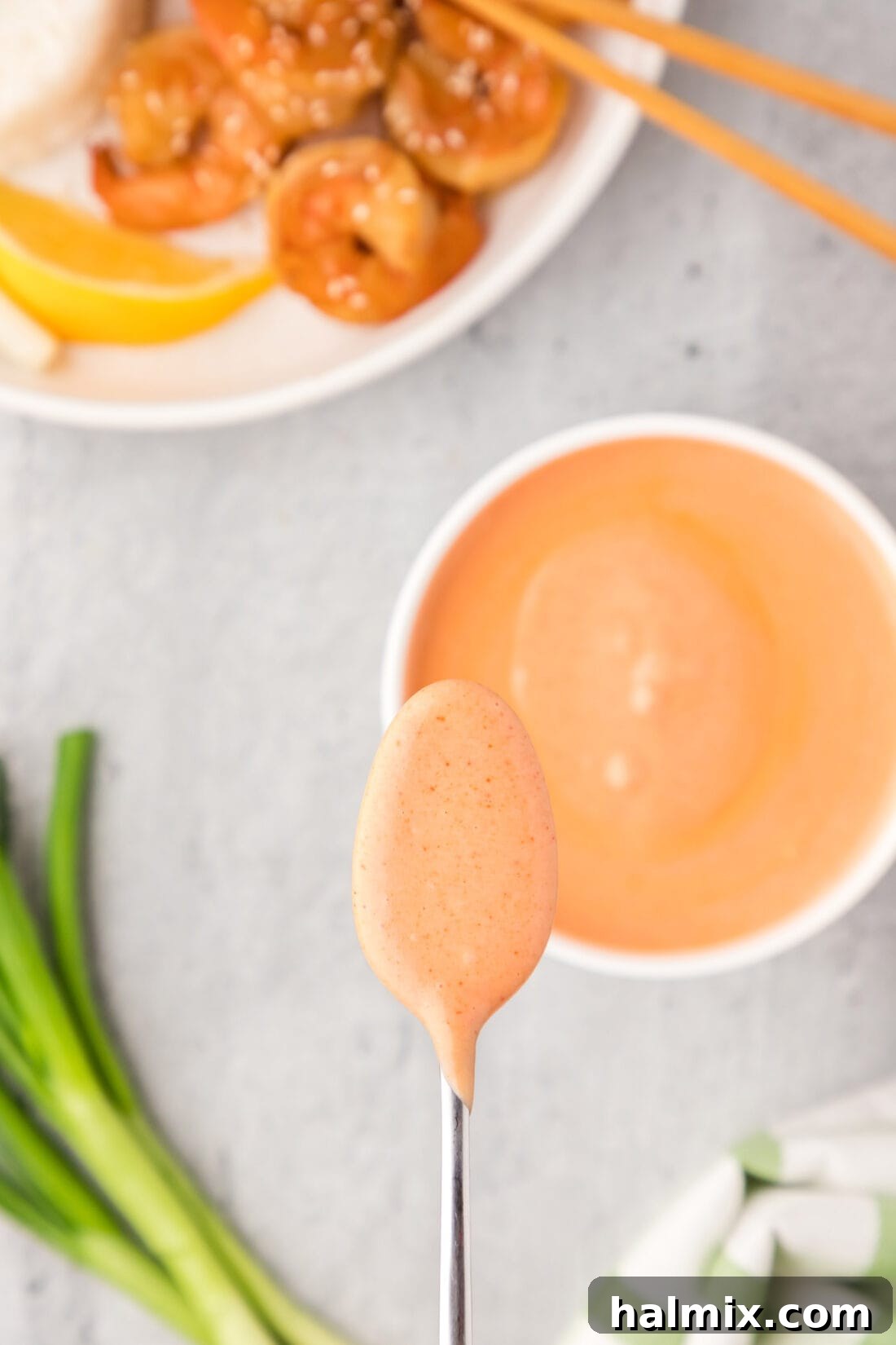 A spoonful of Yum Yum Sauce held over a bowl of the sauce, ready to be served or drizzled.