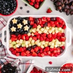Red White & Blue Fruit Salad in a white serving dish surrounded by fruit