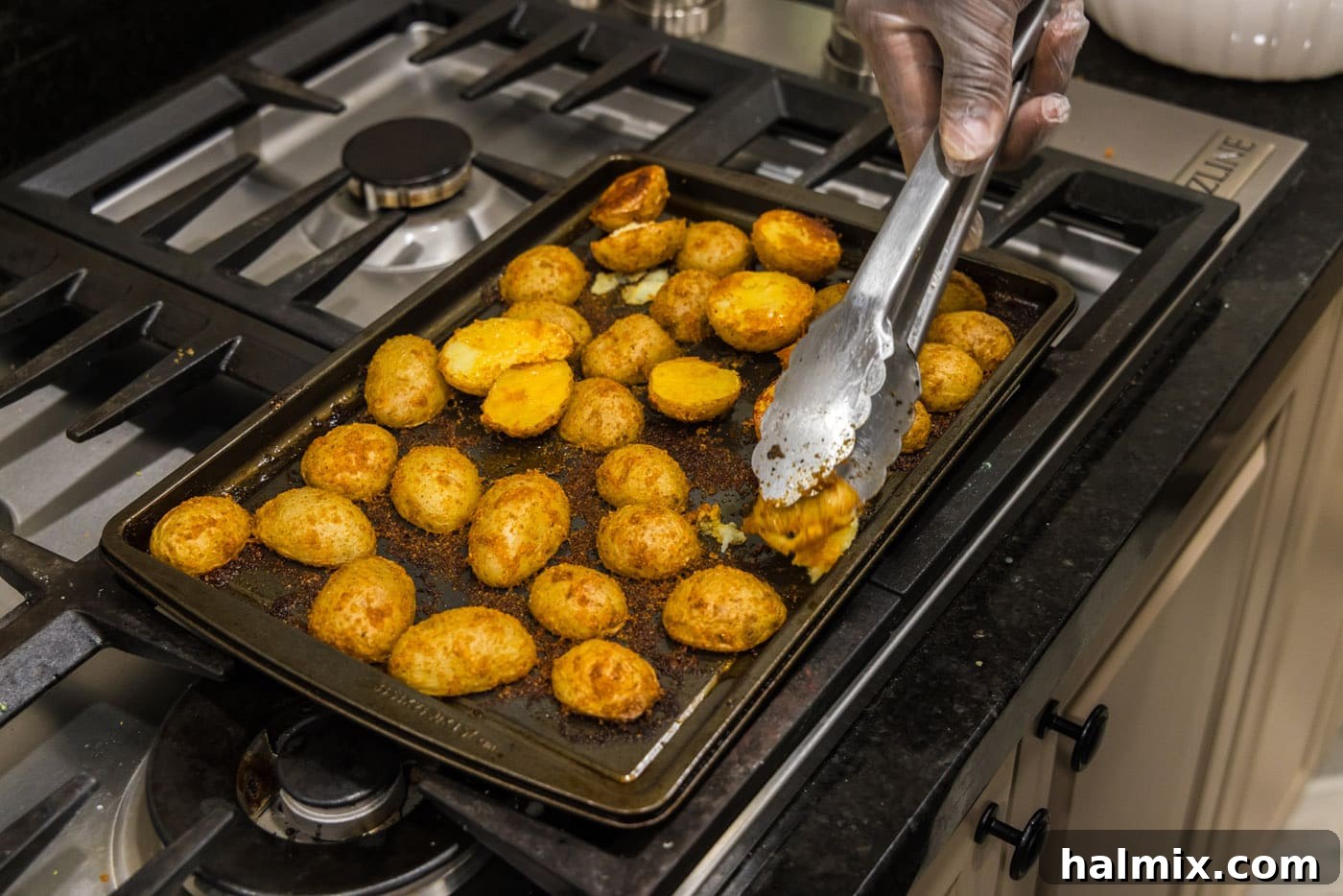 Tongs flipping sliced potatoes on a baking sheet to roast the other side