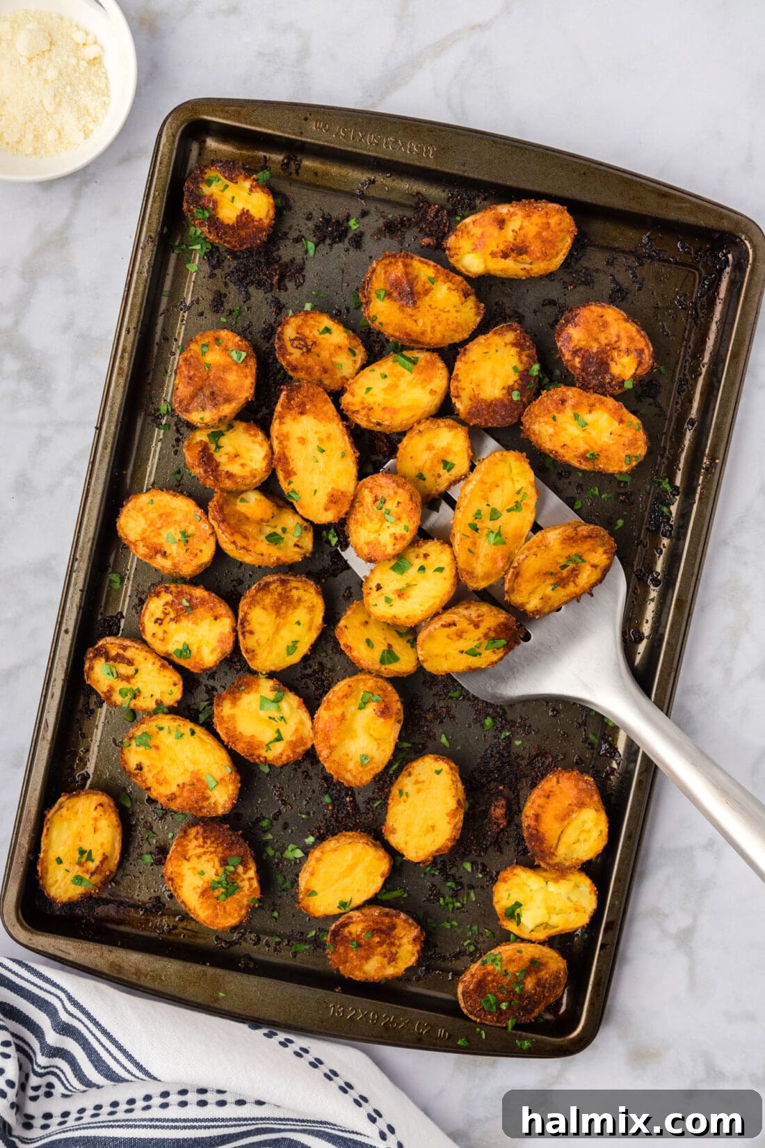A sheet pan filled with golden-brown crispy roasted Parmesan potatoes, garnished with fresh herbs