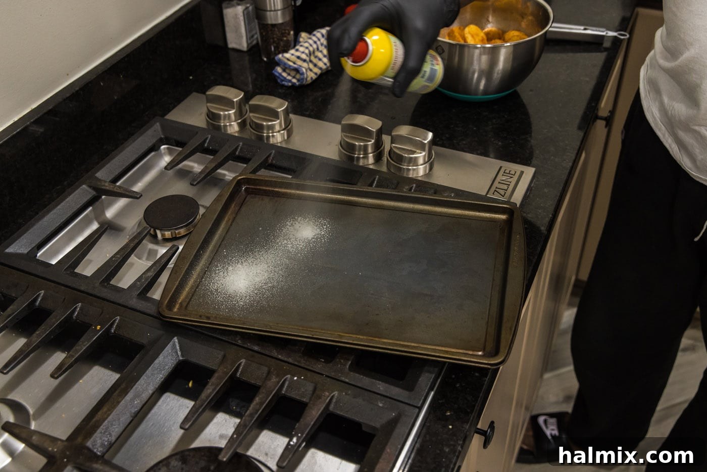 Spraying a baking sheet with cooking spray to prepare for roasting
