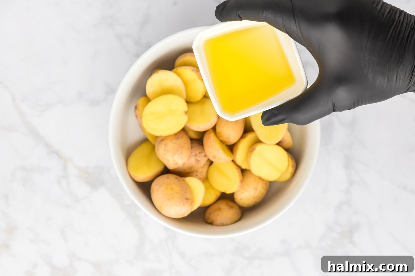 Olive oil being poured over sliced potatoes in a bowl