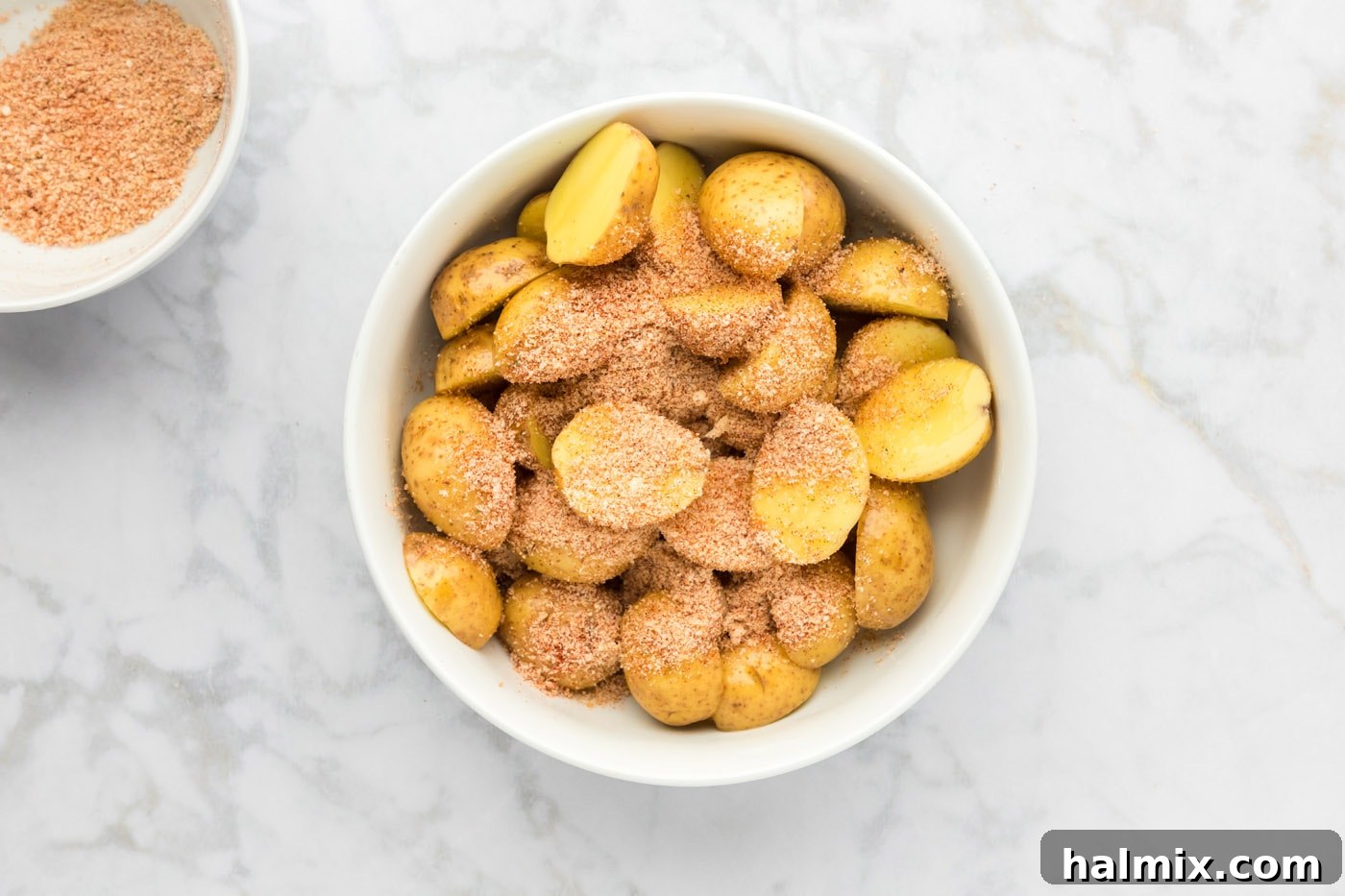 Parmesan seasoning mixture sprinkled over olive oil-coated sliced potatoes in a bowl