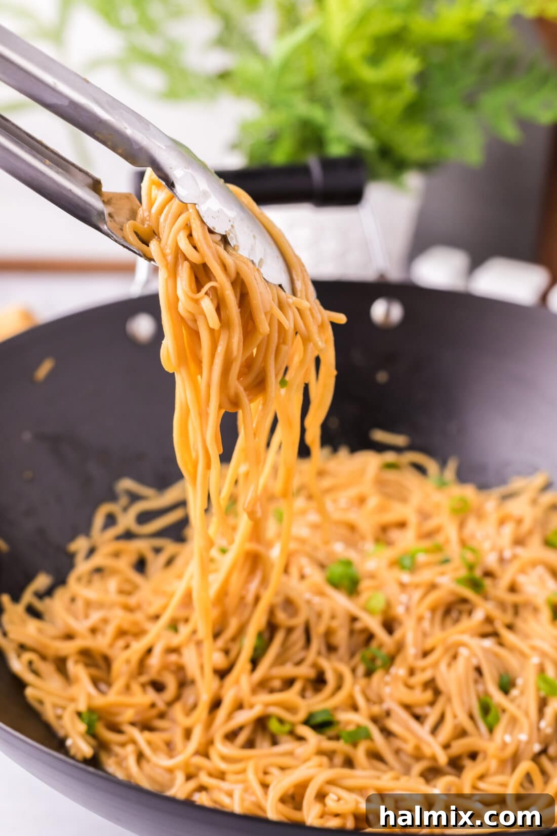 Tongs lifting a generous portion of glistening Teriyaki Noodles from a hot wok