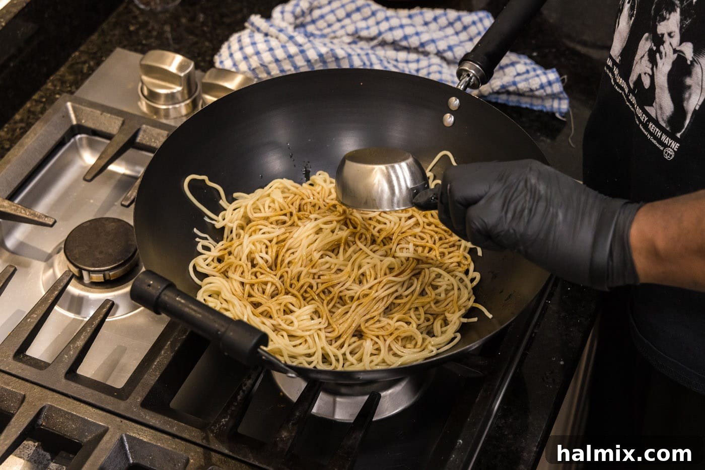 Adding homemade teriyaki sauce to lo mein noodles in a wok