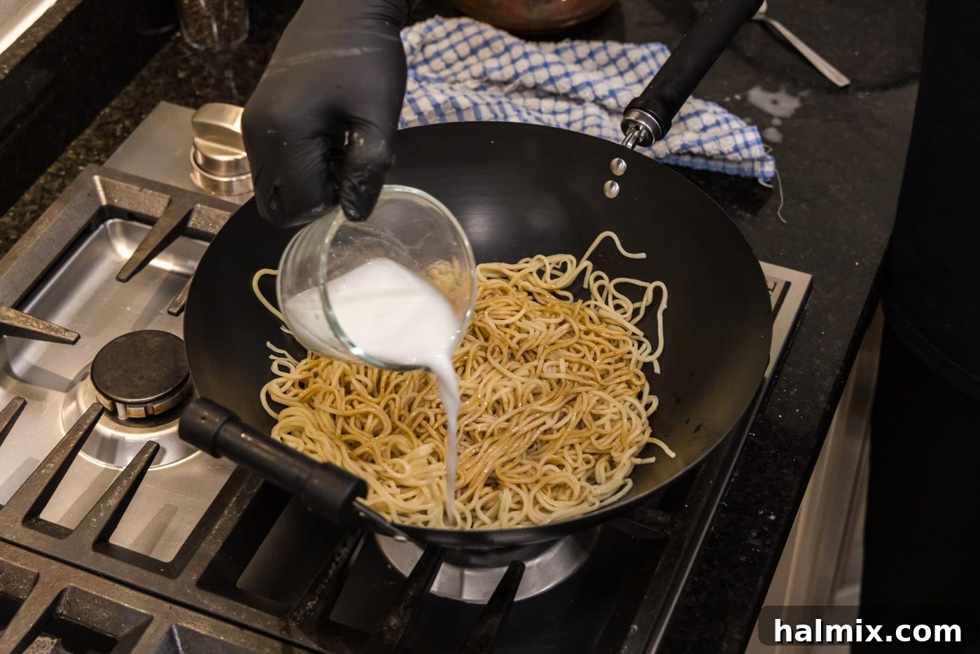 Pouring a cornstarch slurry into teriyaki noodles in a wok