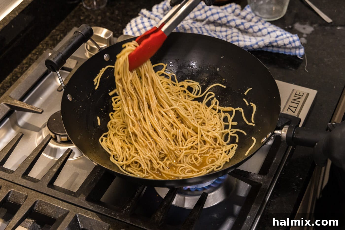Tongs picking up thickened teriyaki noodles from a wok, ready to be served