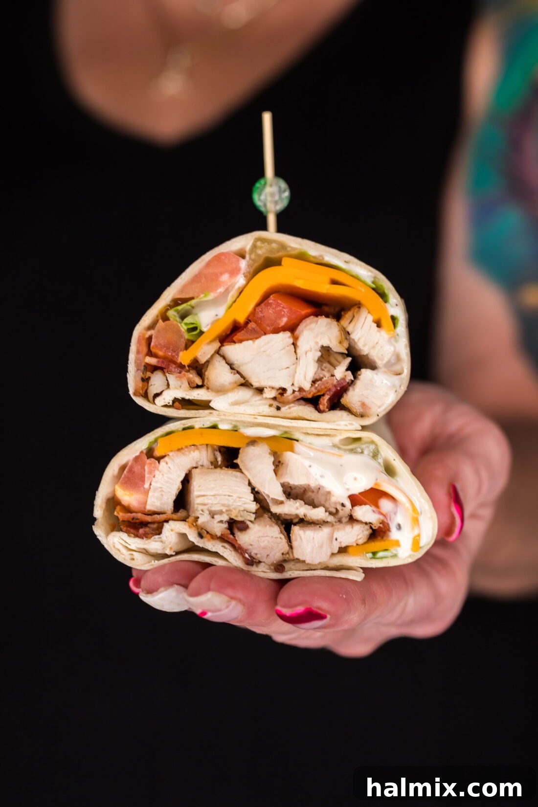 Hand holding two halves of a Chicken Bacon Ranch Wrap stacked on top of each other