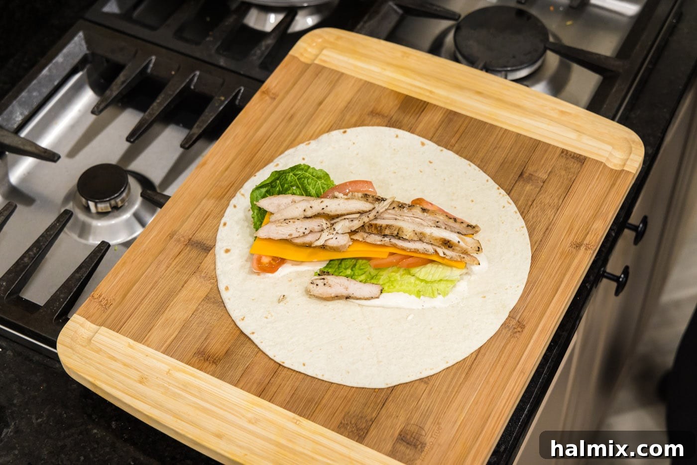 sliced chicken on top of lettuce, ranch, tomato, and cheese wrap