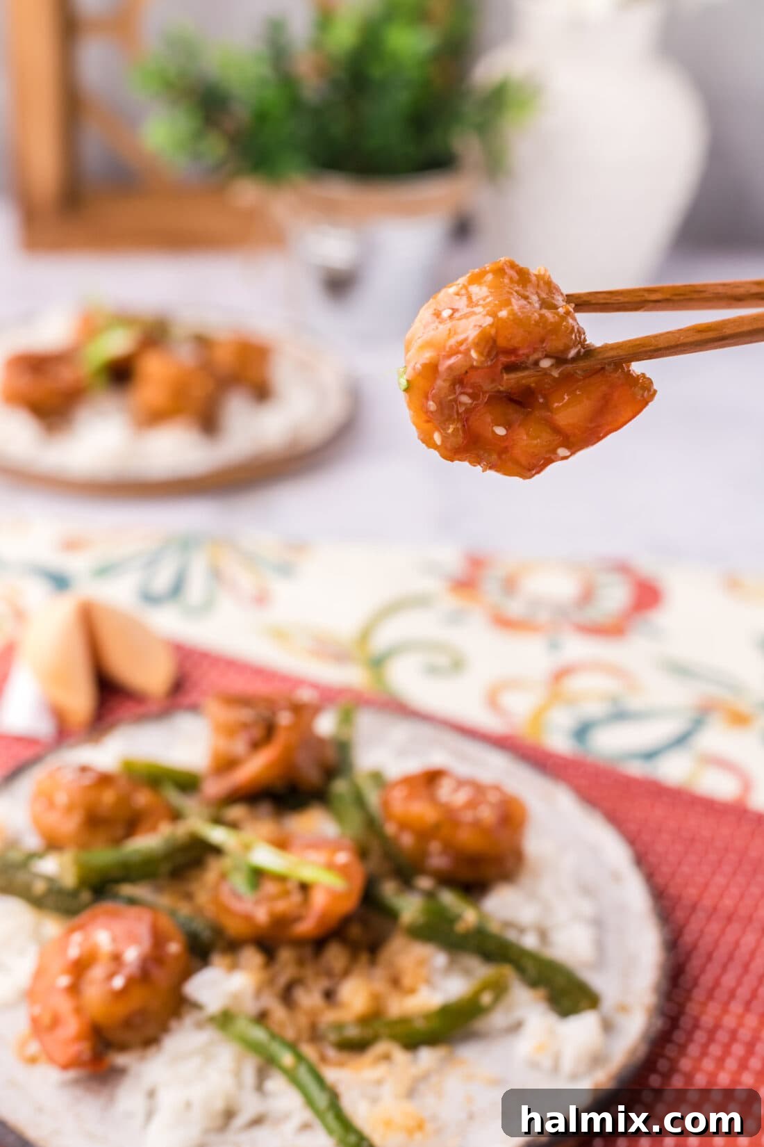 Chopsticks holding a single piece of Hunan Shrimp, highlighting its perfect glaze and inviting texture.