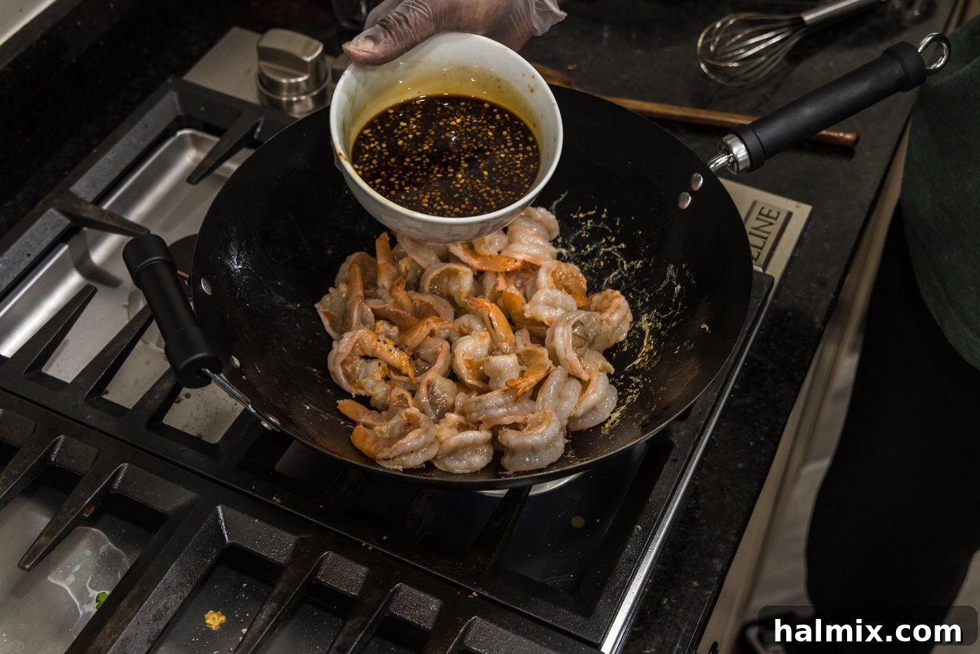Adding homemade Hunan sauce to the stir-fried shrimp in the wok, coating each piece evenly.