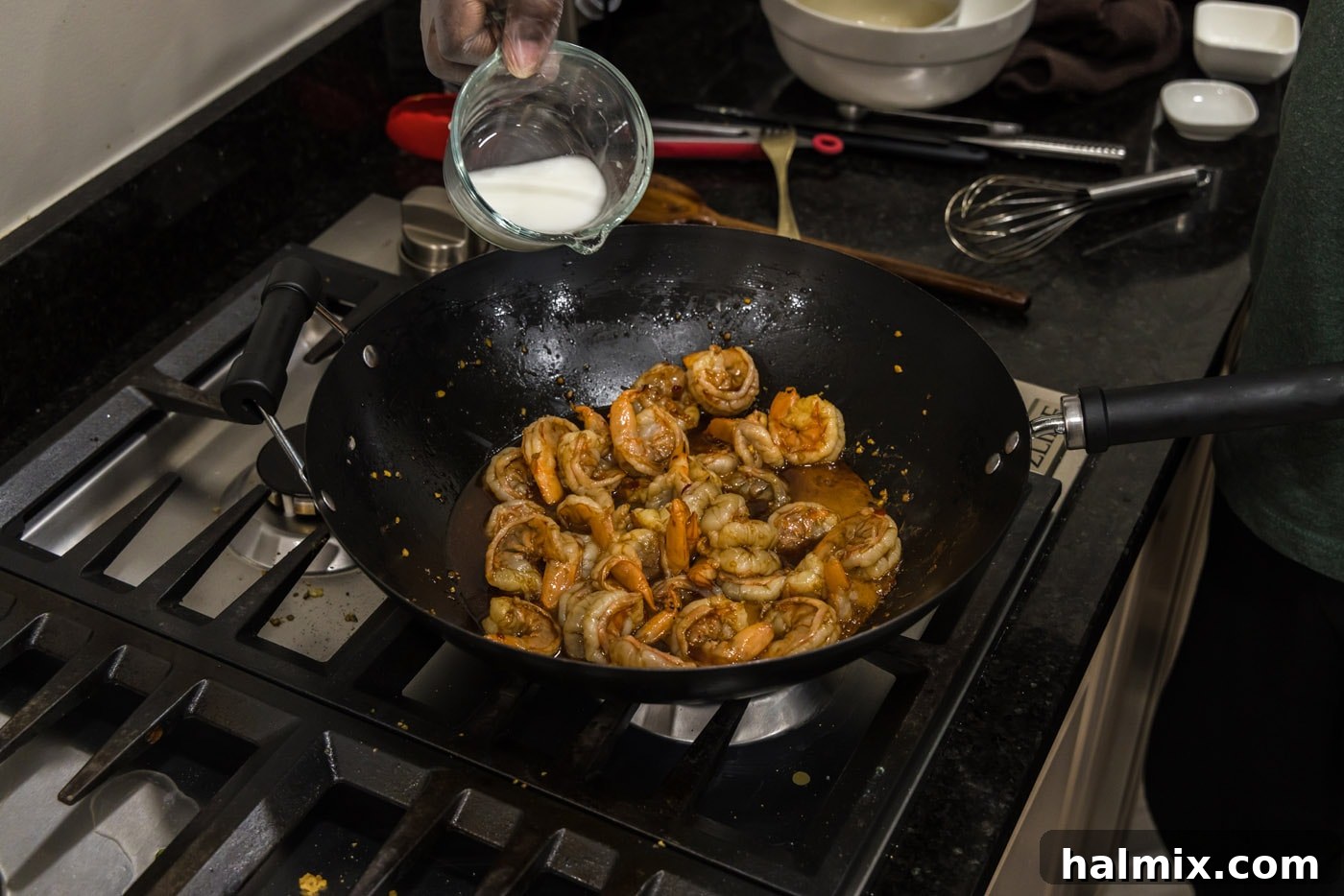 Pouring a cornstarch slurry into the Hunan shrimp and sauce, creating a rich, glossy finish.
