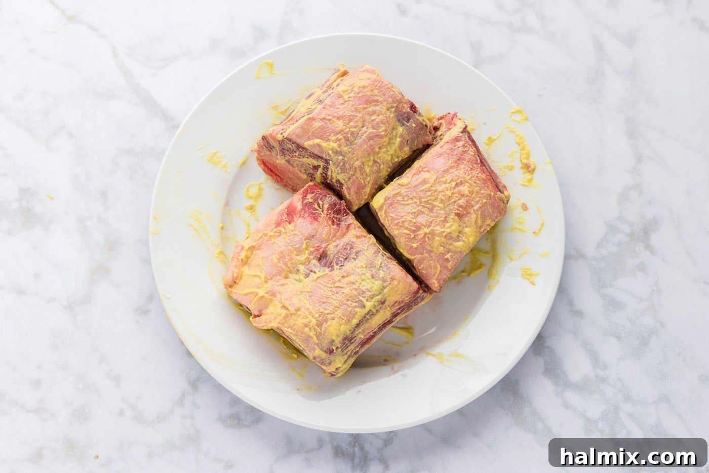 Beef short ribs being coated in Dijon mustard before the spice rub application.