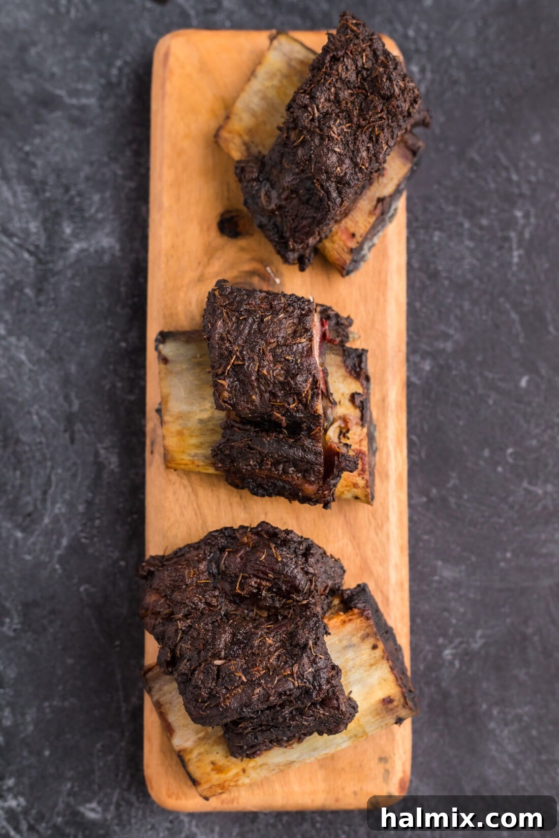 Three perfectly smoked beef short ribs presented on a rustic wooden serving platter.