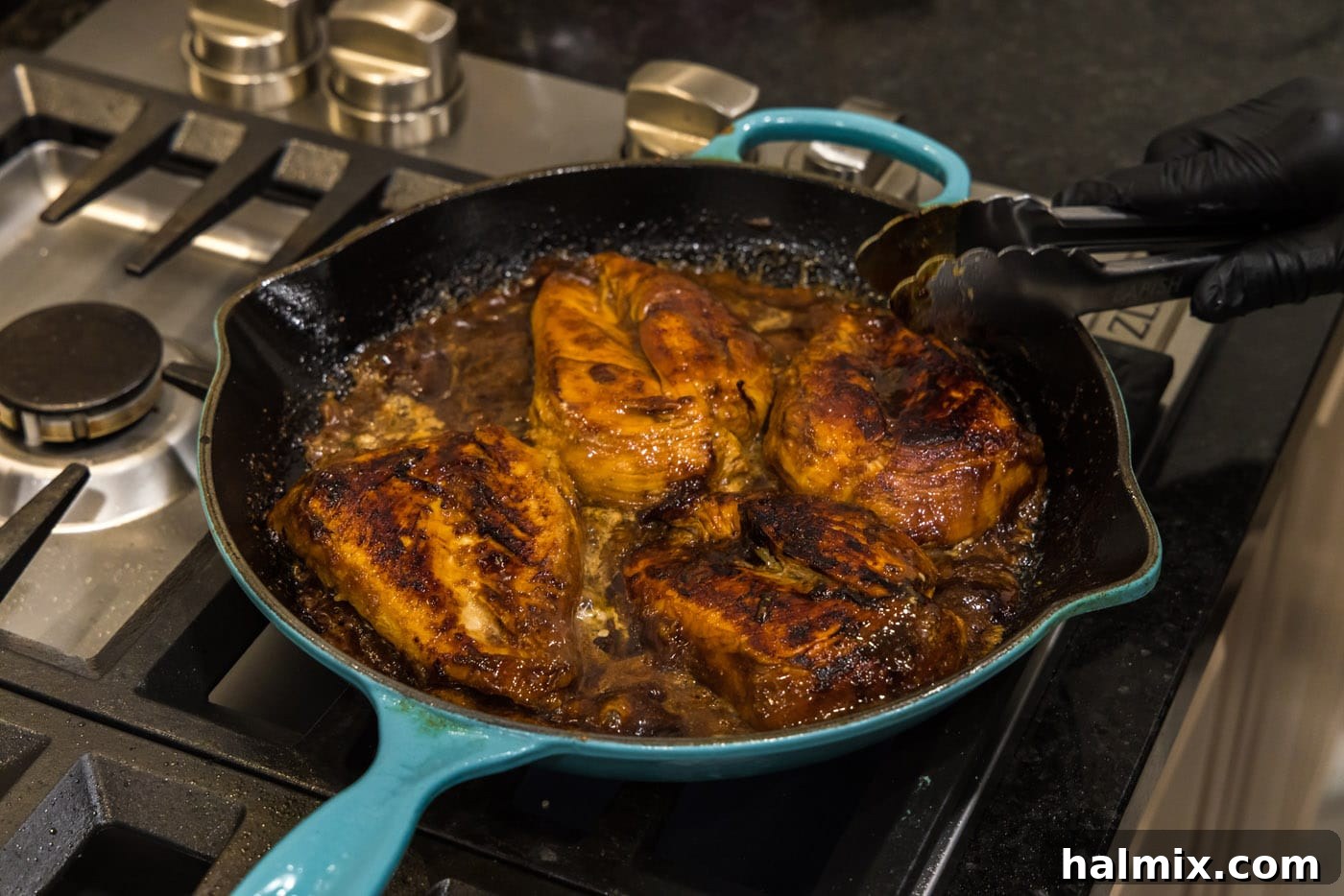 Honey garlic chicken breasts fully coated in a sticky sauce in a skillet, ready for the oven.