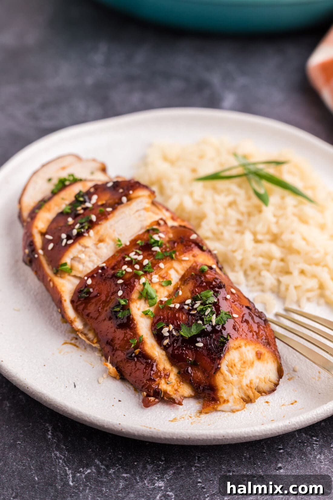 Sliced Honey Garlic Chicken Breast on a plate with rice and green garnish.