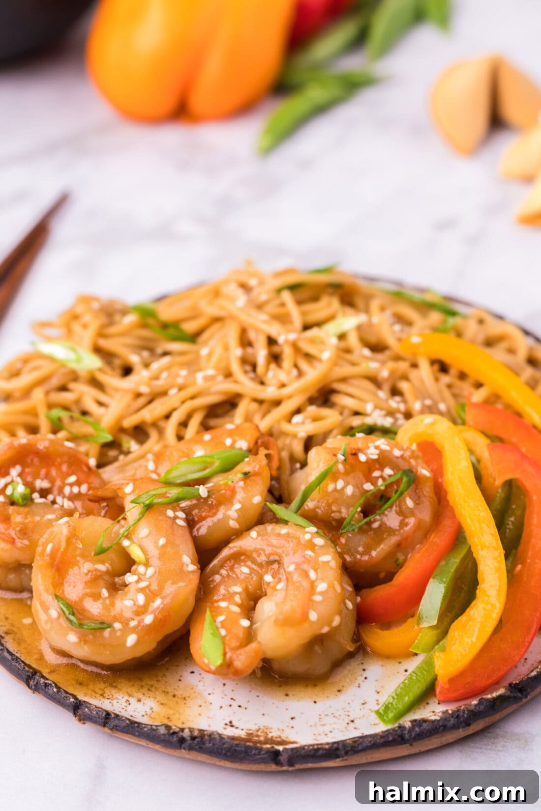 Sticky Teriyaki Shrimp 3 Teriyaki Shrimp served on a plate with a side of teriyaki noodles and thinly sliced peppers, garnished with sesame seeds.