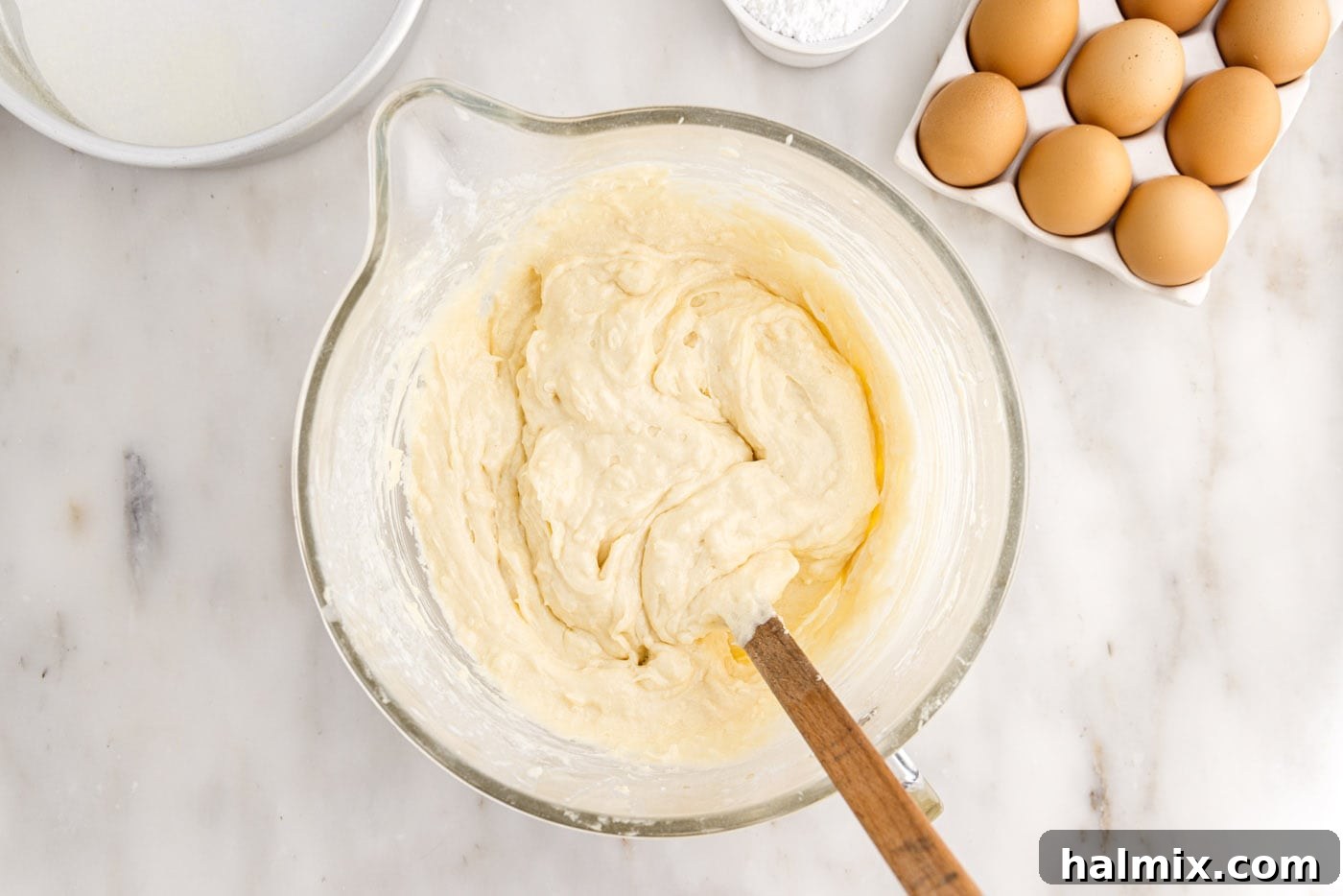 The finished coconut cake batter resting in a large mixing bowl, showcasing its smooth texture with visible shredded coconut pieces.