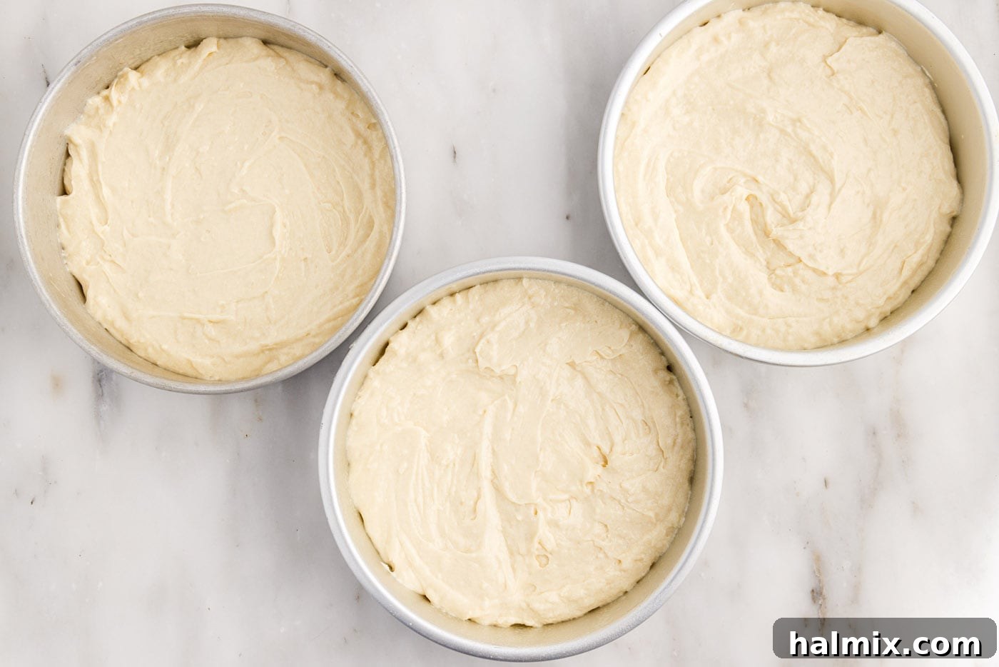 Coconut cake batter evenly divided into three prepared 8-inch round cake pans, ready for baking.