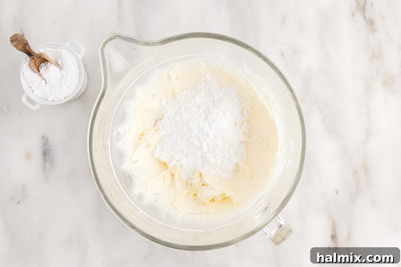 Powdered sugar being added gradually to the creamed butter and cream cheese mixture in a bowl, for making smooth frosting.