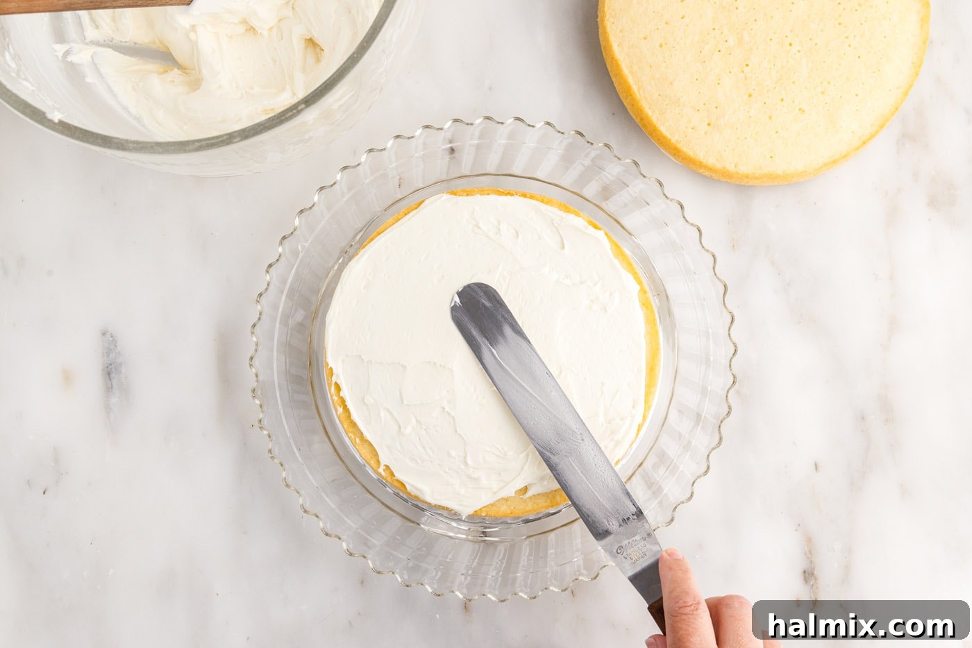 Smooth cream cheese frosting being spread evenly over the top of a coconut cake layer, preparing for the next tier.