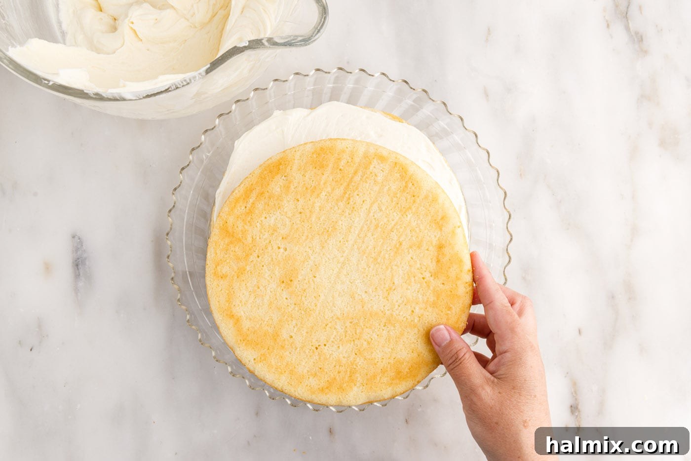 The second layer of baked coconut cake being carefully placed atop the first frosted layer, ready for more frosting.