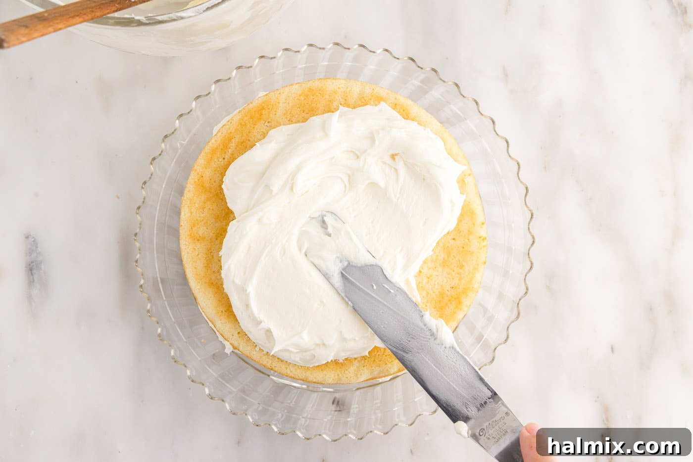 The top of the three-layer coconut cake being frosted smoothly with cream cheese frosting, creating a pristine surface.