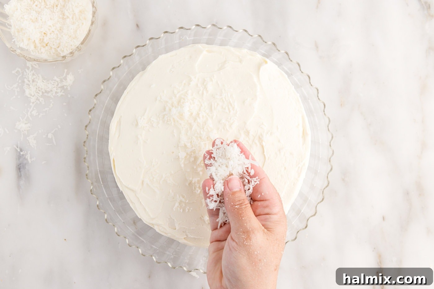 Sweetened shredded coconut being sprinkled generously over the top of a freshly frosted coconut cake, adding texture and flavor.