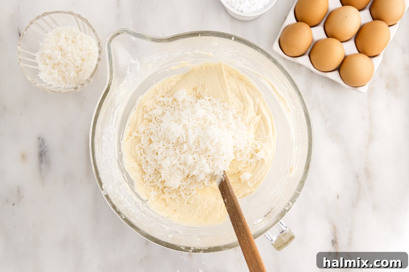 Sweetened shredded coconut being folded into the smooth cake batter, ensuring even distribution for texture and flavor.
