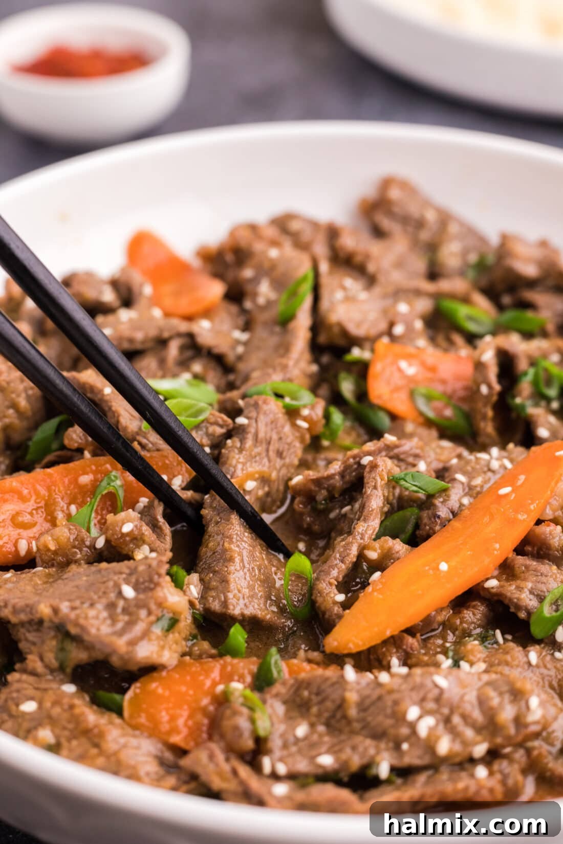 Chopsticks picking up a piece of succulent Beef Bulgogi from a bowl, garnished with sesame seeds.