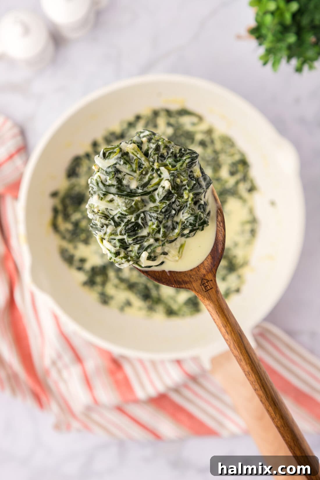 Spoonful of Creamed Spinach held above a skillet of Creamed Spinach
