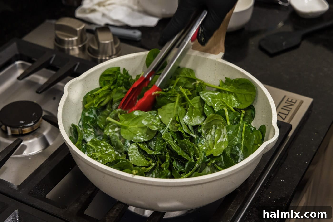 tongs tossing spinach in skillet