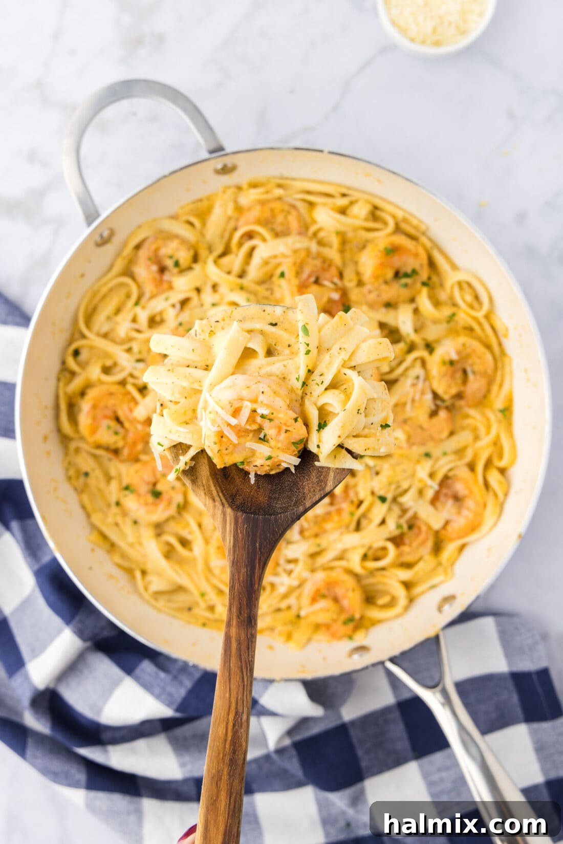 Creamy Garlic Shrimp Alfredo 2 A spoon lifting perfectly cooked Shrimp Alfredo, showcasing plump shrimp and creamy sauce over fettuccine, above a skillet of the dish.