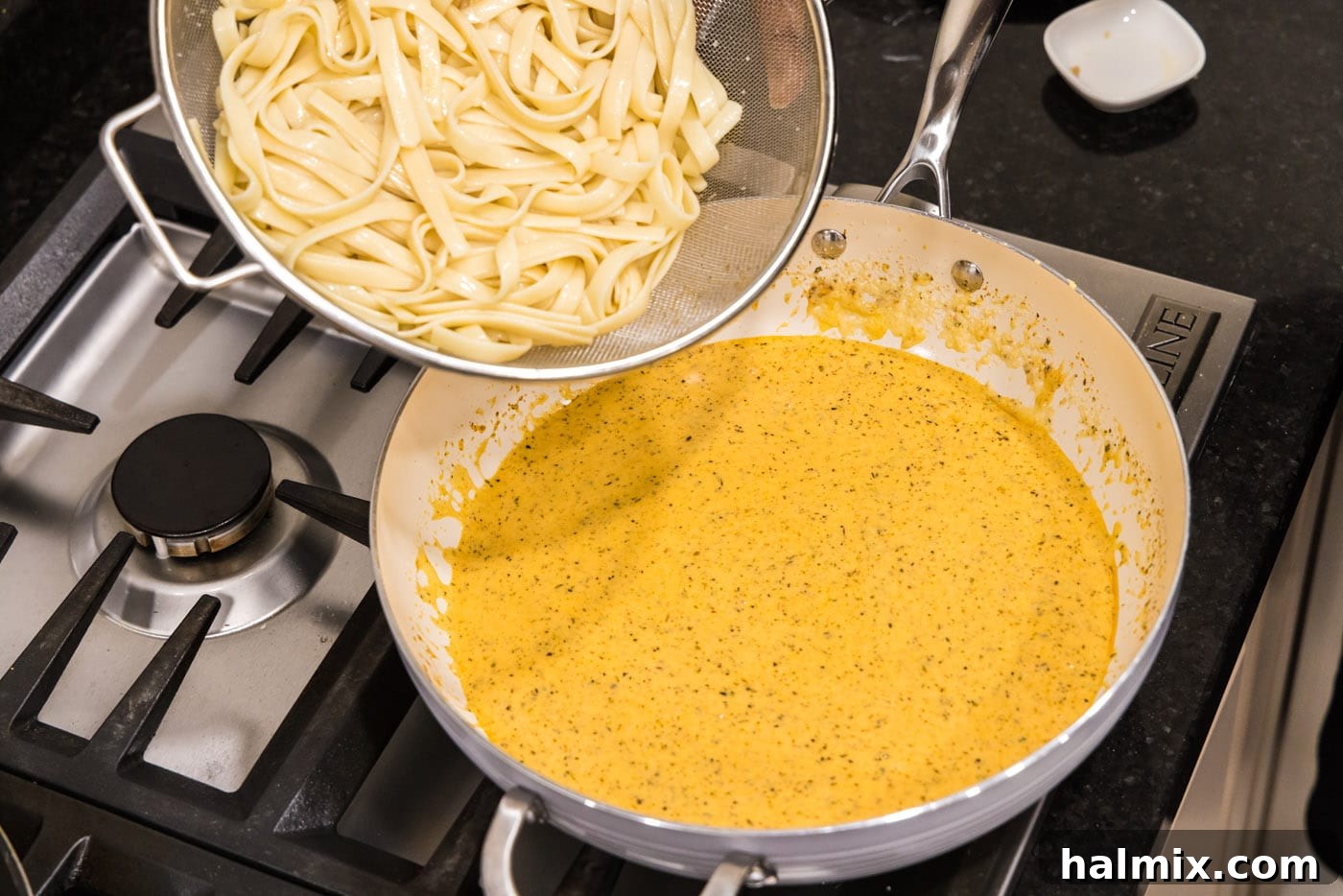Creamy Garlic Shrimp Alfredo 12 Tender fettuccine noodles being added to the creamy Alfredo sauce in a skillet, ready to be tossed.
