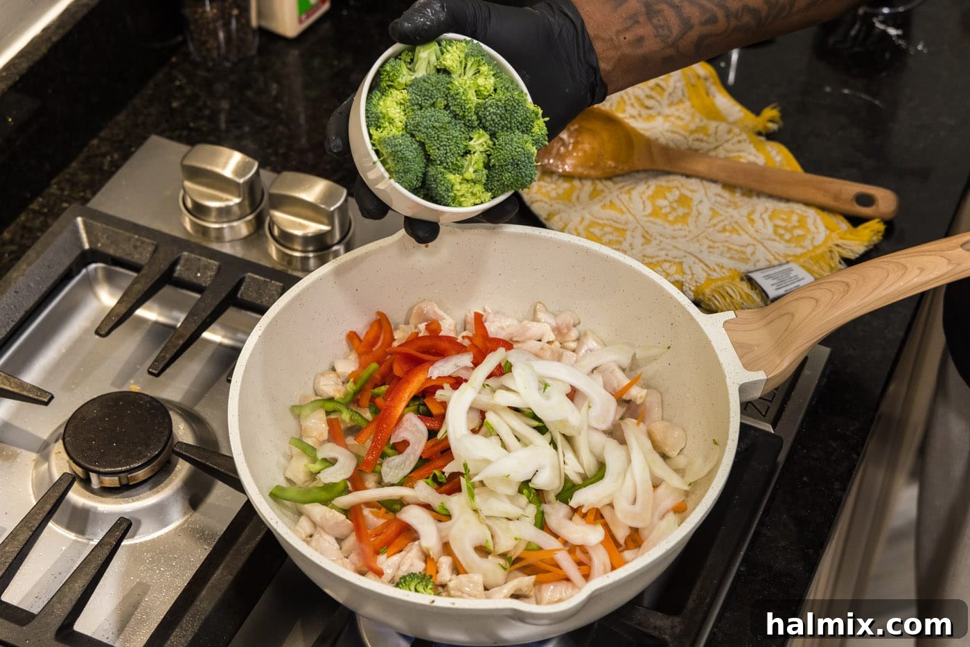 adding broccoli to skillet with vegetables and chicken