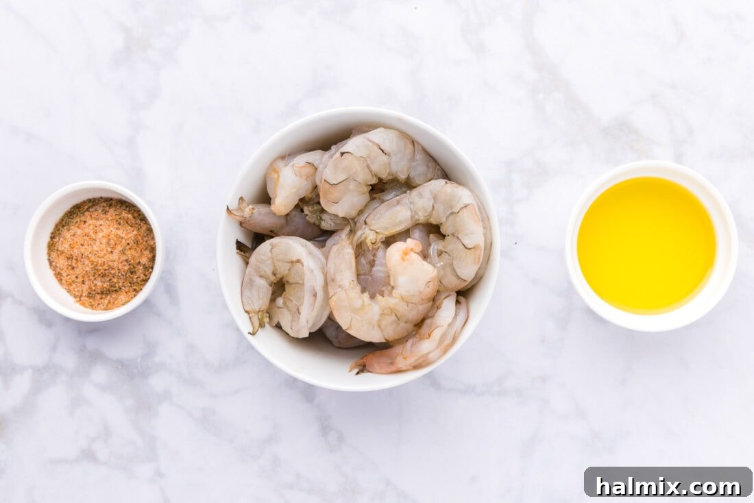 A collection of fresh ingredients laid out for making Cajun shrimp, including raw shrimp, a bowl of seasoning, and a bottle of olive oil.
